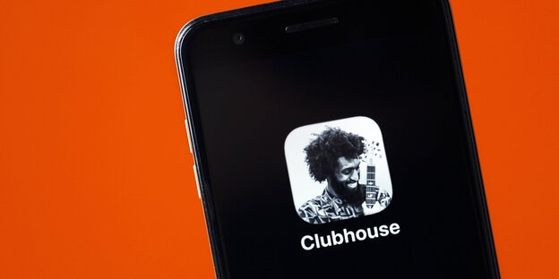 Ein Smartphone vor orangem Hintergrund. Auf dem Bildschirm ist nur das Logo der App Clubhouse zu sehen