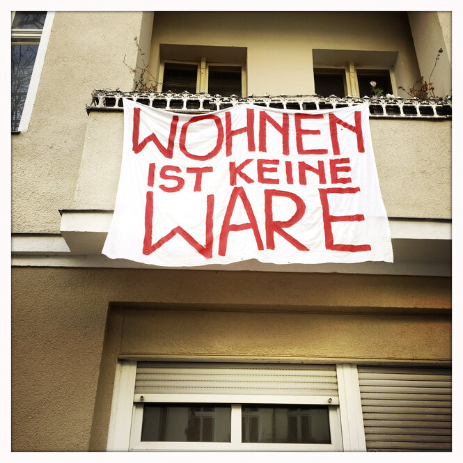 Vom Balkon eines Wohnung hängt ein Tuch mit der Aufschrift "Wohnen ist keine Ware".