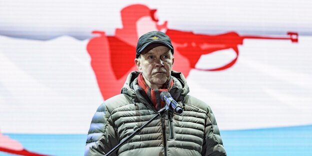 Besseberg, Chef des Biathlon-Weltverbands, vor einem Transparent, auf dem ein Biathlet beim Schießen abgebildet ist.