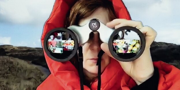 Ein Frau in roten Kapuzenwindjacke hat ein Fernglas vor den Augen