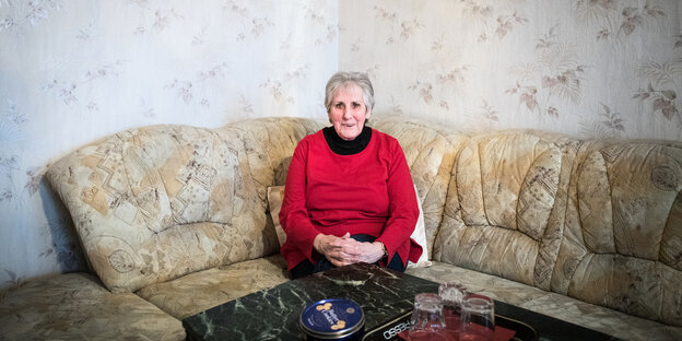 Monika Ziebeil sitzt mit rotem Pullover auf ihrem Sofa