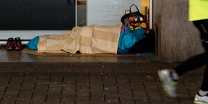 Ein Mensch liegt im Schlafsack im Eingang zu einem Geschäft