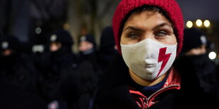 Eine junge Frau mit roter Mütze trägt eine Gesichtsmaske. mit einem roten Blitz, das Protestzeichen gegen Abtreibung