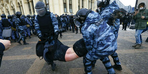 Uniformierte Polizisten tragen einen Demonstrierenden.