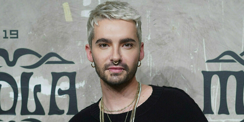 Bill Kaulitz steht vor einer grauen Wand und schaut frontal in die Kamera