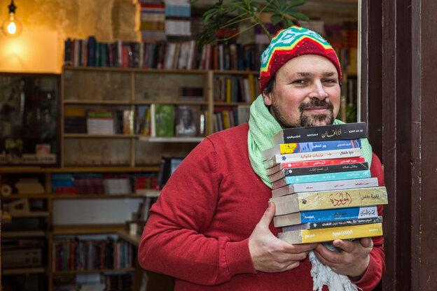 Ein Mann hält einen Stapel arabischer Bücher in die Kamera und lächelt