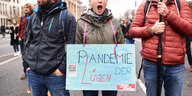 Drei Demonstranten - zwei Männer, eine Frau in der Mitte hält ein Schild mit der Aufschrift "Pandemie der Lügen"