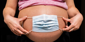 Eine Person hält eine Mundschutzmaske vor ihren schwangeren Bauch