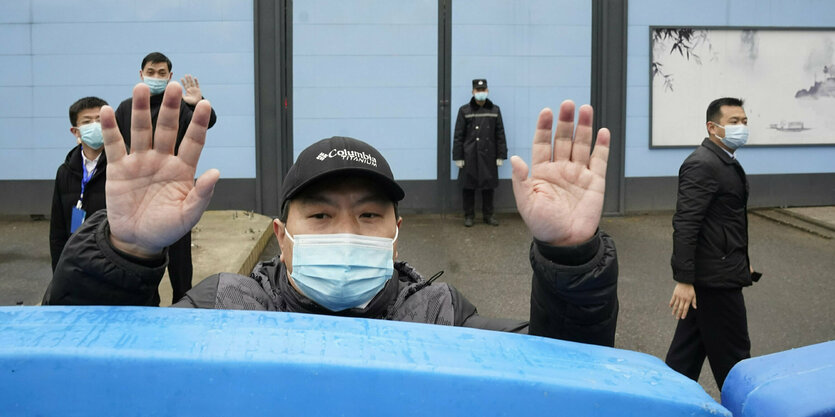 Ein Mann mit Maske macht eine abweisende Handbewegung.