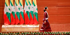 Oppositionsführerin Aung San Suu Kyi neben Flaggen Myanmars läuft von einer Bühne