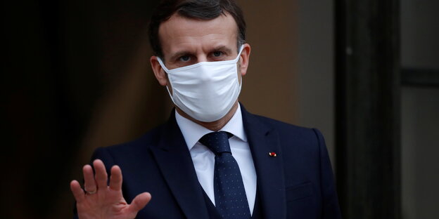 Frankreichs Staatschef Emmanuel Macron mit Mund-Nasenschutz hebt die Hand
