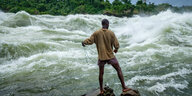 Ein Mann steht an auf einem Felsen an einem reissenden Fluss