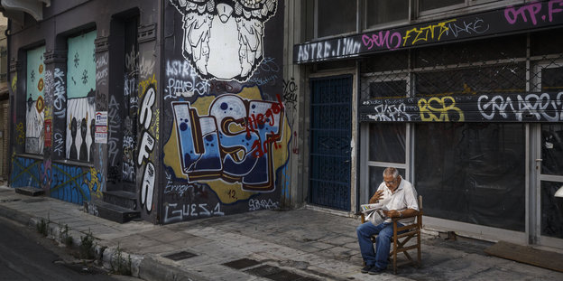 EIn rauchender mann sitzt vor verlassenen Ladengeschäften in Athen