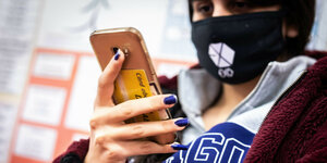 Schülerin mit Maske schaut auf ihr Smartphone