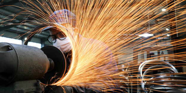 Ein Arbeiter mit gesichtsmaske bei der Bearbeitung von Metallteilen an einem Schleifgerät - es fliegen Funken