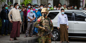 Ein bewaffneter Soldat steht in Yangon vor Bewohnern der Stadt