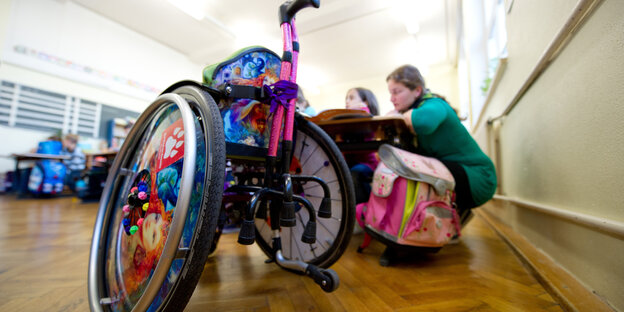 Ein Rollstuhl steht vor einer Schulbank, an der ein Mädchen sitzt