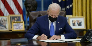Joe Biden sitzt mit Mundschutz an Schreibtisch und schreibt