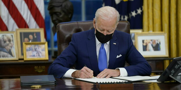 Joe Biden sitzt mit Mundschutz an Schreibtisch und schreibt