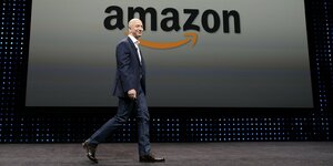 Jeff Bezos geht auf einer Bühne mit dem Firmenlogo von Amazon im Hintergrund
