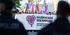 Polizisten begleiten einen Protestmarsch von Antifa-Demonstranten, die ein Banner mit der Aufschrift „Nazimacker bekämpfen, Antifaschismus in die Offensive“ tragen.