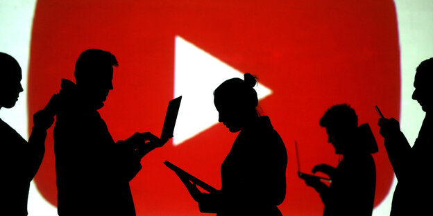 Silhouetten von Menschen mit Laptops und Smartphones vo einem großen youtube Logo