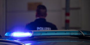 Vor einem üsterreichischen Polizeifahrzeug mit Blaulicht läuft ein Polizist