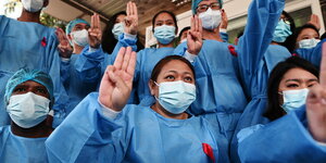 Krankenhauspersonal in Yangon in blauer Arbeitskleidung mit roten Schleifen heben ihre Hände