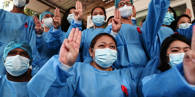 Krankenhauspersonal in Yangon in blauer Arbeitskleidung mit roten Schleifen heben ihre Hände