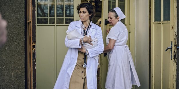 Nina Kunzendorf trägt in der Rolle als Kinderärztin Dr. Ingeborg Rapoport ein Baby vor einem Krankenhaus