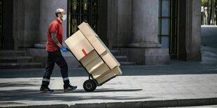 Ein Mann schiebt eine mit Pakten beladene Sackkarre auf dem Gehweg