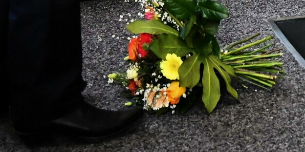 Ein Blumenstrauß vor den Schuhen eines Mannes