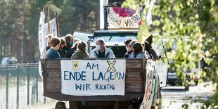 Auf einem offenen LKW sitzen mehrere Menschen. Ein Plakat hinten auf dem LKW trägt die Aufschrift "Am Ende lage(r)n wir richtig".