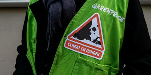 Klimaaktivist con Greenpeace mit grüner Weste und Sticker mit der Aufschrift "Klima in Gefahr" (auf französisch)