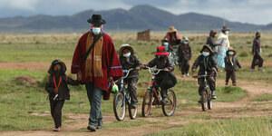 Aymara-Indigene mit ihren Kindern, alle tragen Gesichtsmasken, drei Kinder sind auf dem Fahrrad unterwegs