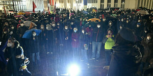 Dutzende Demonstranten mit Mund-Nasenschutz und Regenschirmen in Wien