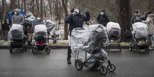 mehrere Frauen mit Kinderwagen stehen mit Abstand und Maske vor der Innenbehörde. Eine spricht aufgebracht in eine Mikro