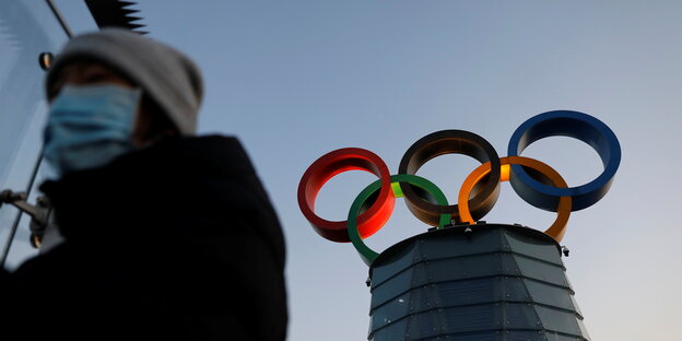 Eine Bürgerin mit Gesichtsmaske vor dem Olympischen Turm in Peking