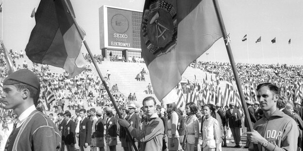 Zwei Männer tragen je eine Fahne, DDR und BRD, im Stadion