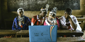 tVier Mädchen sitzen in einer Schule in Kenia vor einem Bildschirm und schauen sich etwas an, das sie emotional mitzunehmen scheint. Zwei verdecken sich die Augen