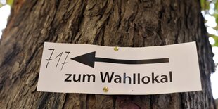 Schild an einem Baum, das ins Wahllokal weist.