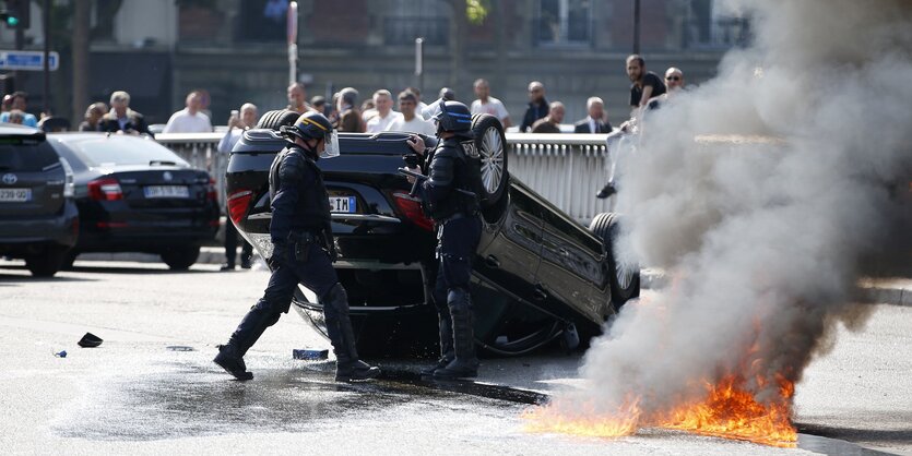 Polizisten neben einem umgekippten Auto.