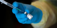 Eine Hand im Schutzhandschuh hält ein Fläschchen mit Impfserum