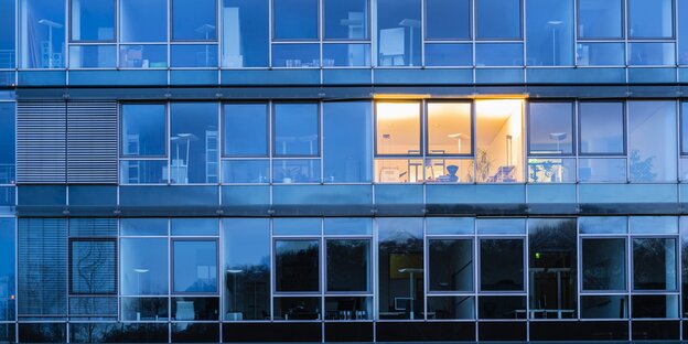 Glasassade eines Bürogebäudes, in einem einzelnen Fenster brennt Licht