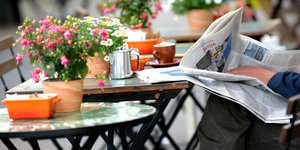 Ein Mann sitzt mit Zeitung vor einem Straßencafé.