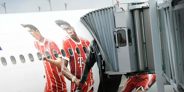 Ein Flugzeug am Flughafen. Auf der Flugzeugwand sind Bilder von Spielern des FC Bayern München zu sehen