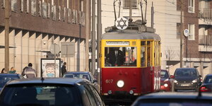 Eine rot-gelb gestrichene historische Straßenbahn mit Daivstern inmittem dem Alltagsverkehrs von Warschu