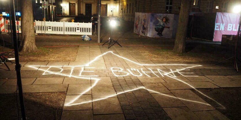 Auf der nächtlichen Straße unter dem Licht der Laterne ist ein Stern auf das Trottoir gemalt und die Buchstaben "Die Bühne"