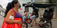 eine Frau mit einer Atemmaske in den Straßen von Havanna. Über der Schulter trägt sie eine Tasche, aus der eine Katze schaut