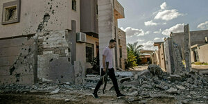 Ein Mann mit Geweht geht an einem zerstörten Gebäude vorbei